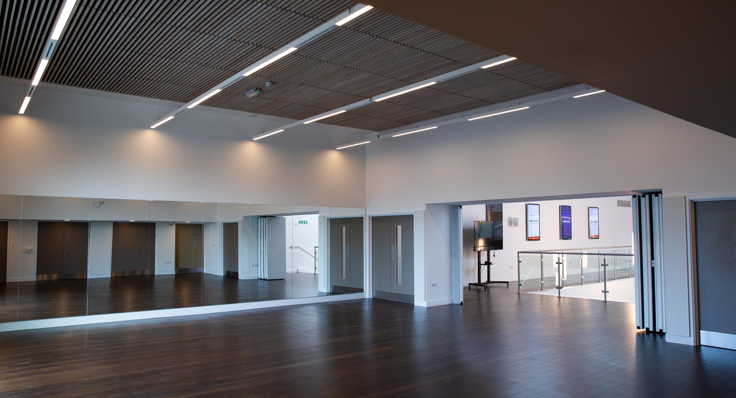 An empty brightly sunlit room with mirrors along one side, looking out onto a interior balcony of the rest of the venue.
