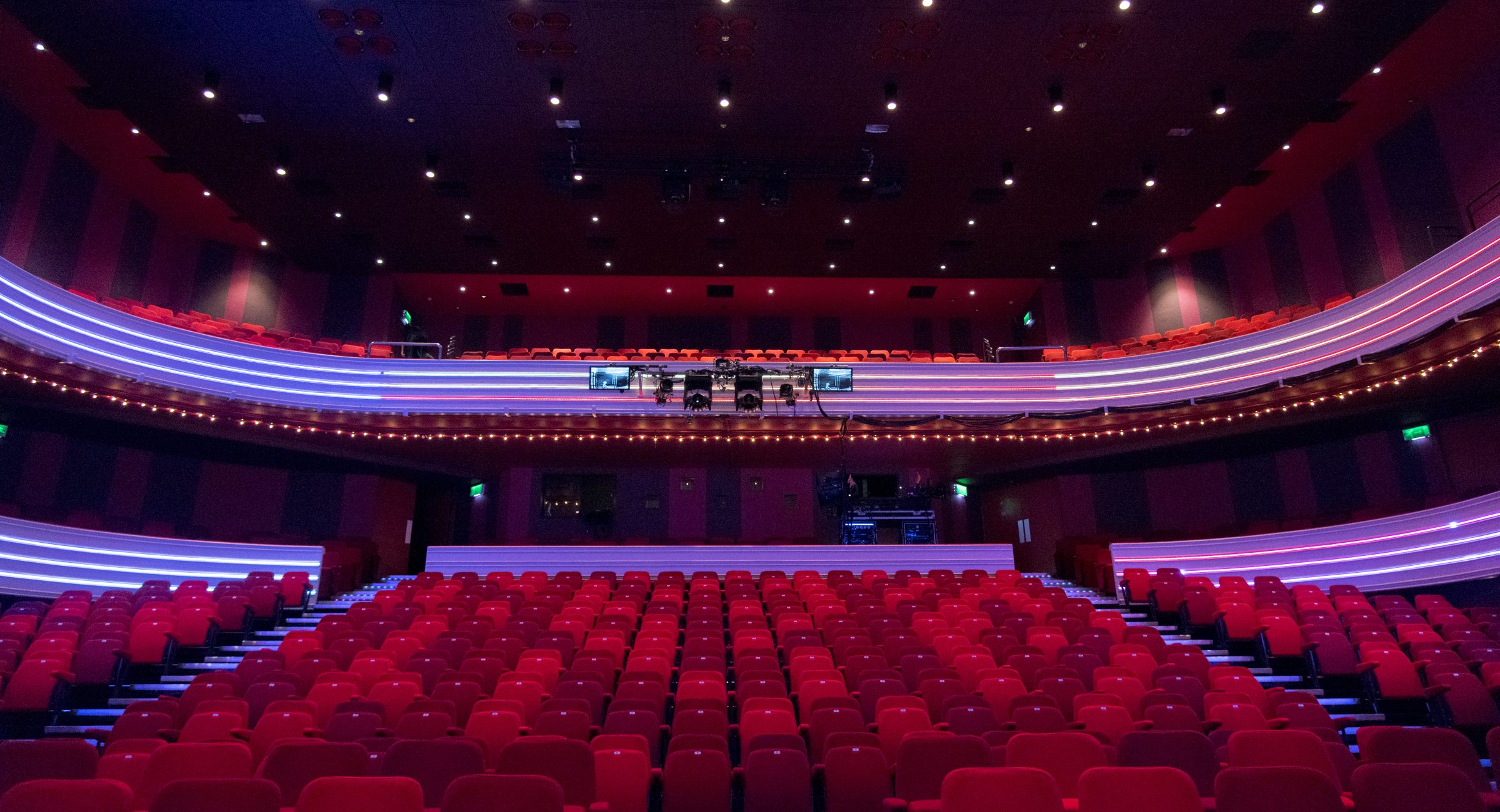 A shot of the auditorium tiered red chairs and white lit balcony.