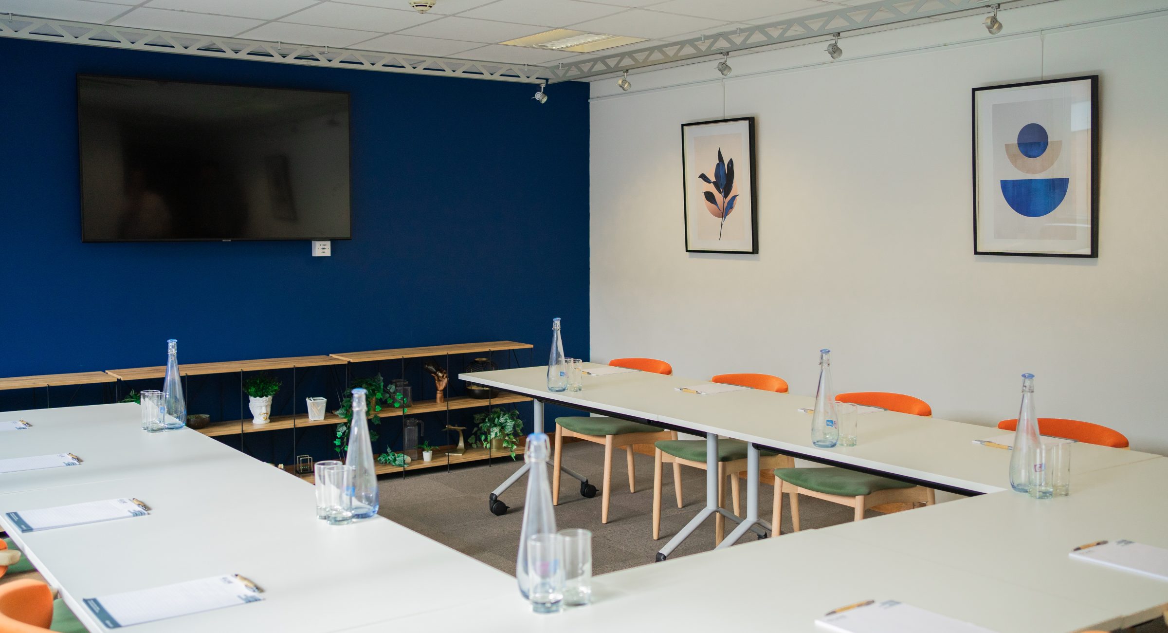 White U shape conference table set up with note pads and blue wall it the background.