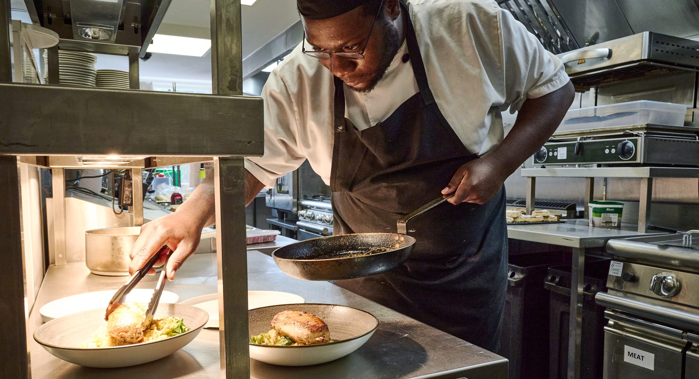 A chef in whites plating a dish of food on the pass.