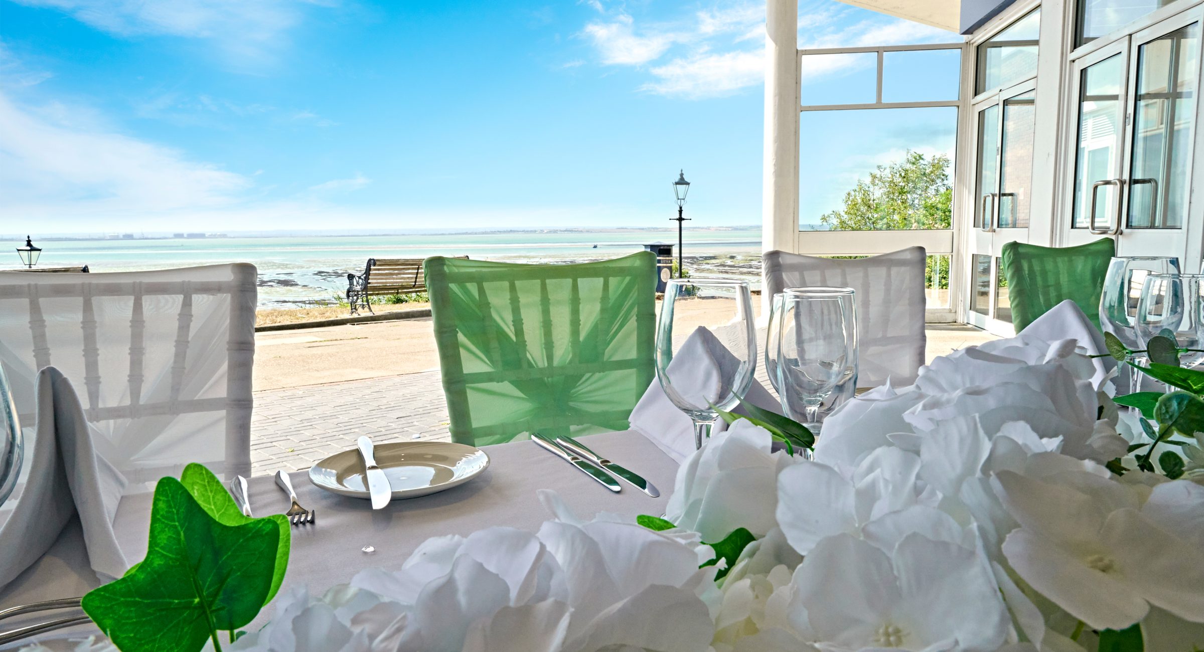 Elegant floral arrangement on a fully laid up top table of a wedding, looking out at the sea.