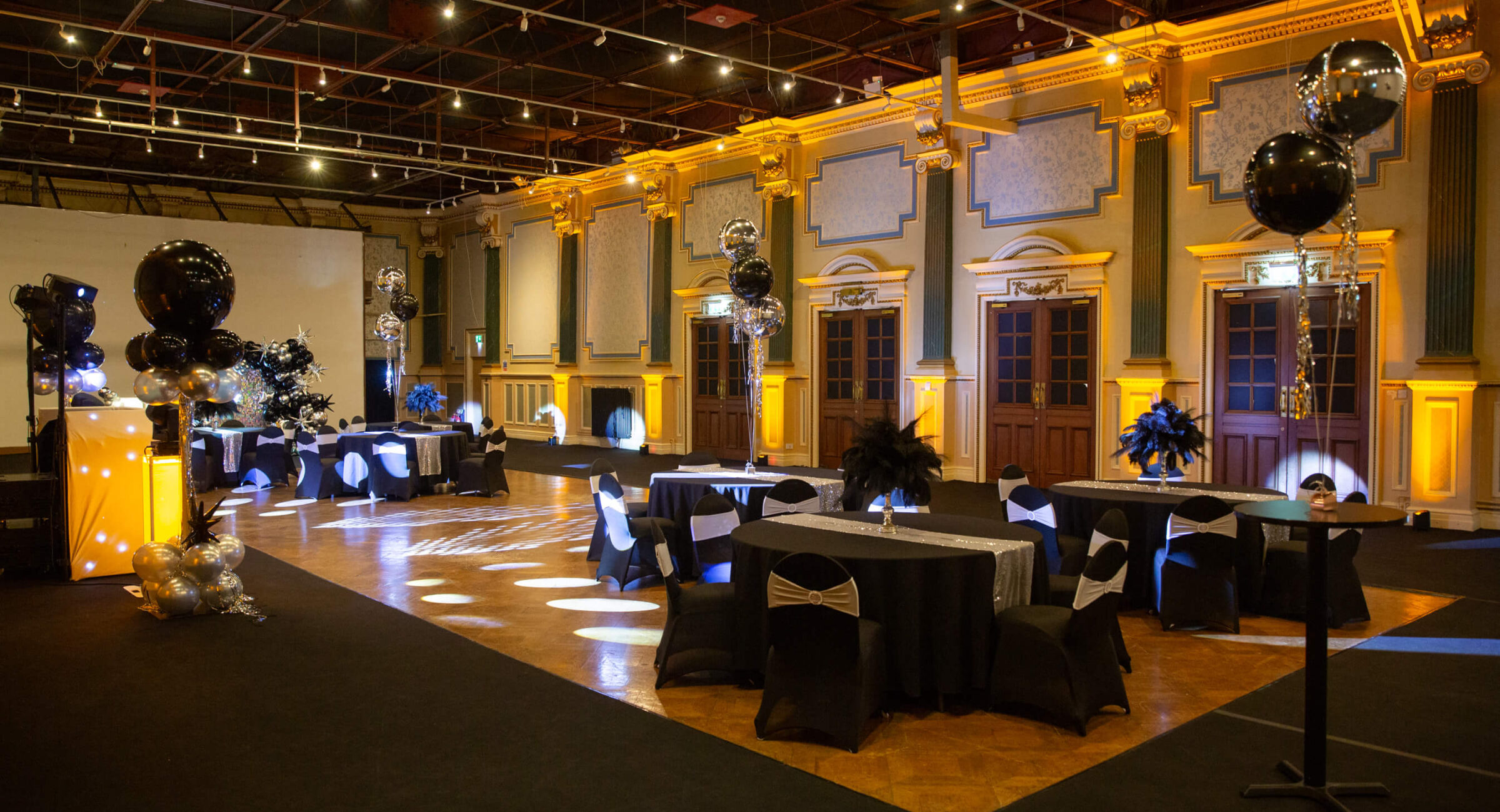 The Gold room set up as a party with black tables with feather centrepieces and chairs, gold uplighters along the walls.